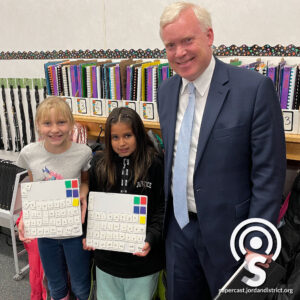 Superintendent stands with two students showing their work